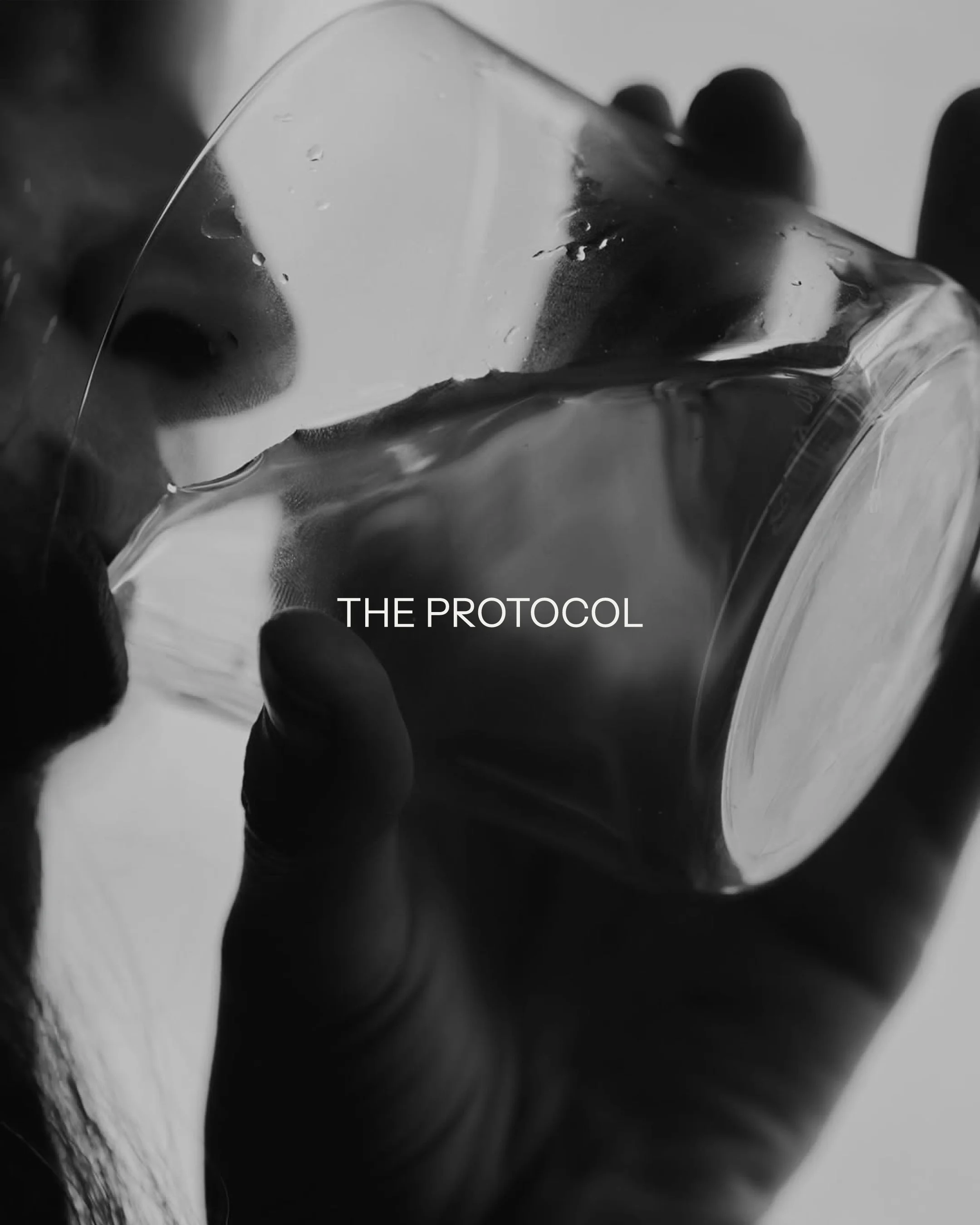 Una mano sostiene un vaso de vidrio, con «The Protocol» sobreimpreso, en blanco y negro.