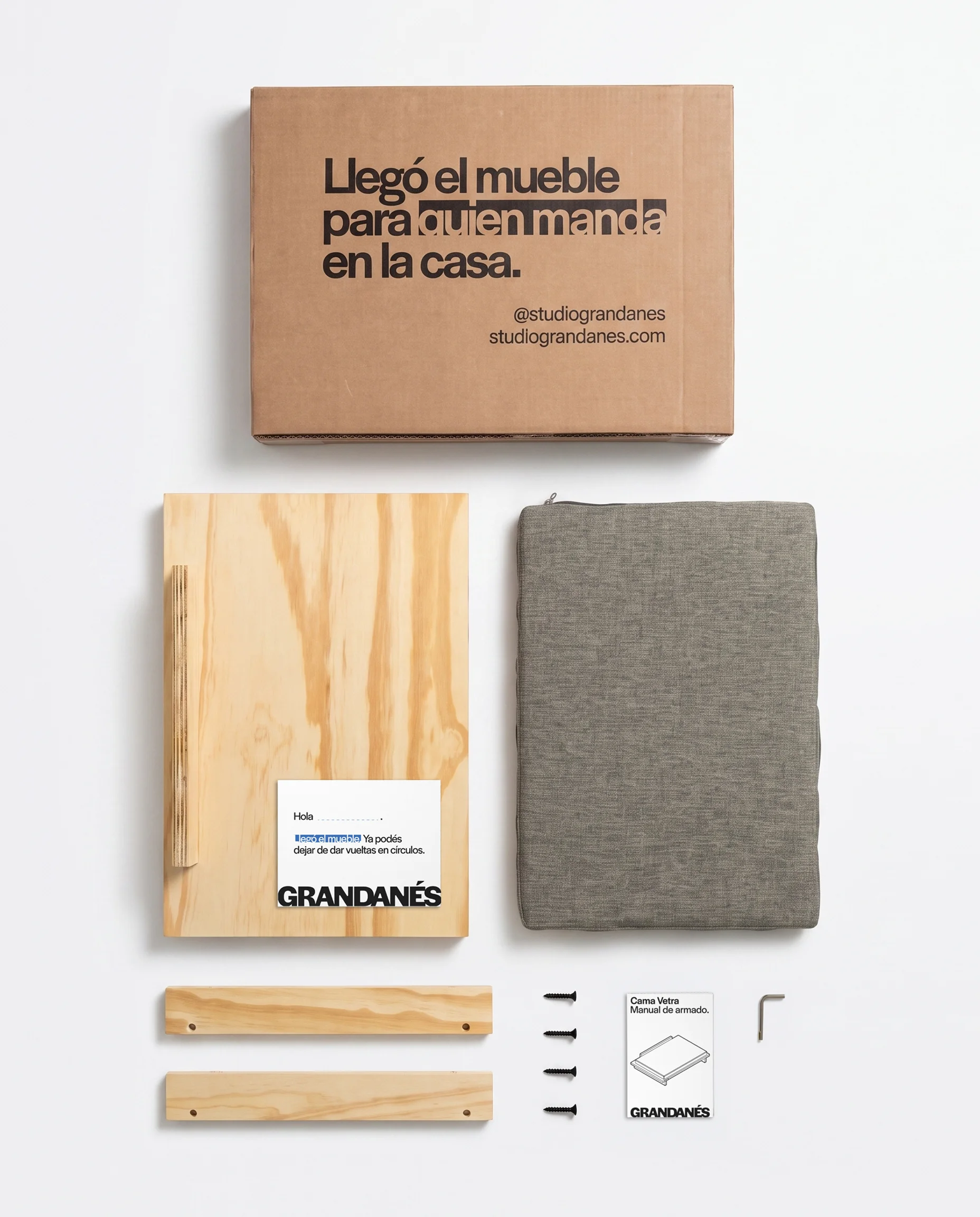 El contenido de la caja desplegado: el cartón «Llegó el mueble para quien manda en la casa», las piezas de madera, el almohadón, los tornillos y el manual.